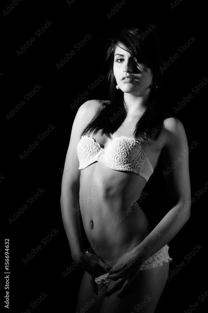 black and white or monochrome image of young beautiful slim woman posing nude in white underwear and touching her pussy