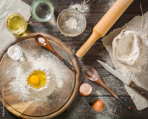 Ingredients for cooking dough or bread. Broken egg on top of a bunch of white rye flour. Dark wooden background.