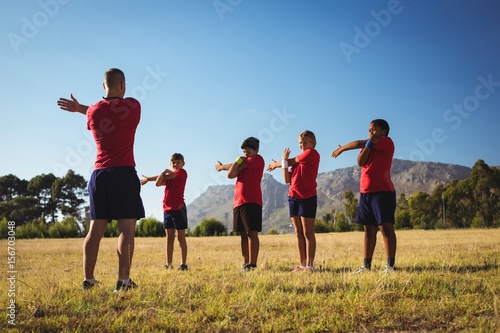 Male trainer instructing kids while exercising in the boot camp