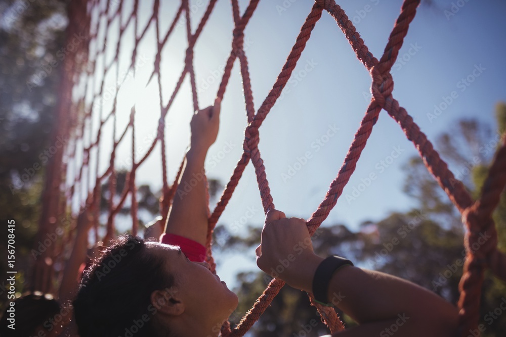 Fototapeta premium Fit woman climbing a net during obstacle course training