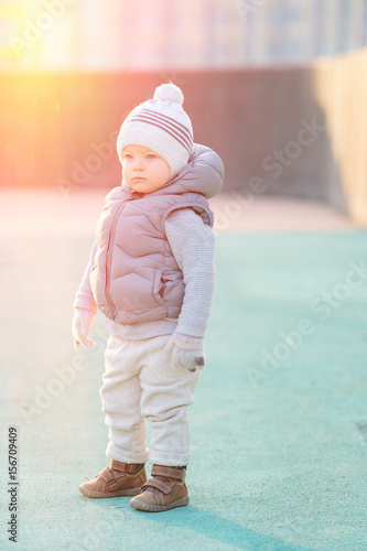 Toddler child in warm vest jacket outdoors. Baby boy at playground during sunset.