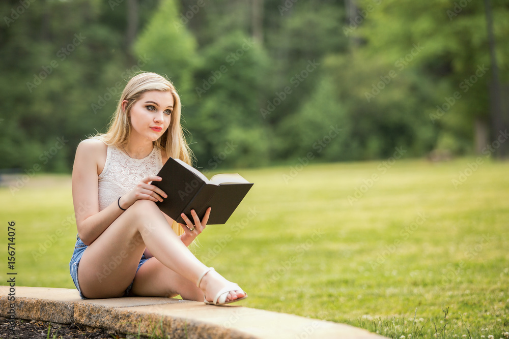 Obraz premium Teenage girl with a book in the park during the summer.