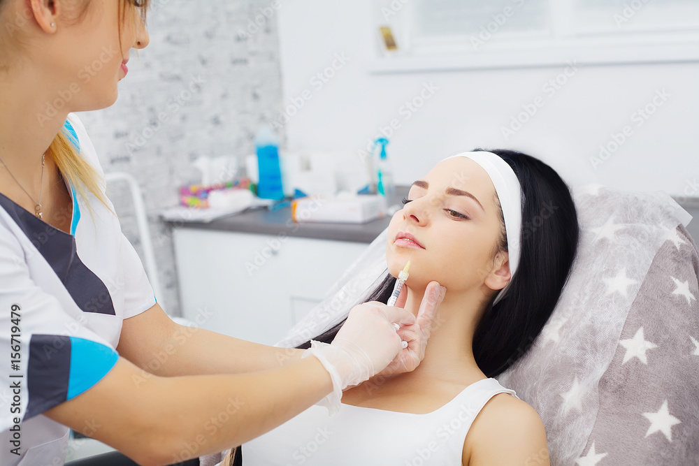 Woman receiving a botox injection in the lips zone lying in bathrobe on the medical couch