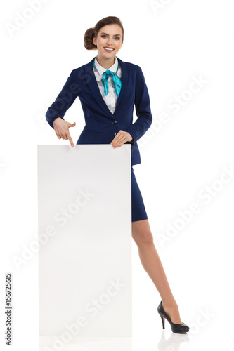 Smiling Stewardess Is Standing Behind Poster Amd Pointing On It