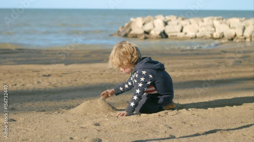 The boy is building a mountain of sand on the beach.