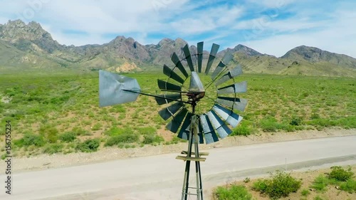Aerial Flying Over Old Spinning Windmill. a drone view flying over an old windmill spinning with a desert and large mountain range in the background. Slow motion
