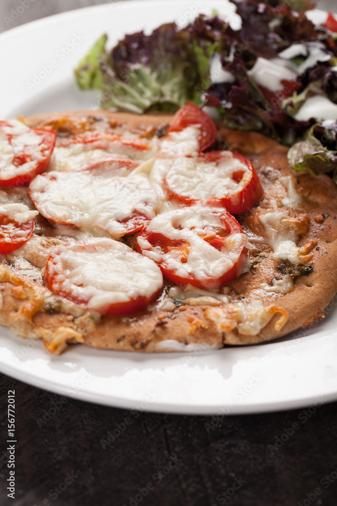Homemade pizza with marinara sauce topped with parmesan cheese and sliced tomatoes with a side salad up close shot
Homemade pizza with marinara sauce topped with parmesan cheese and sliced tomatoes with a side salad up close shot