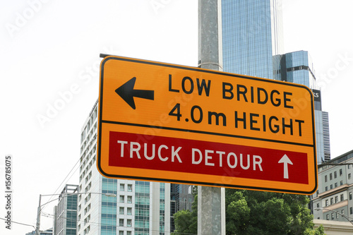 A yellow and black ’Low Bridge, 4m Height’ and ‘Truck Detour’ sign near the entrance to a bridge