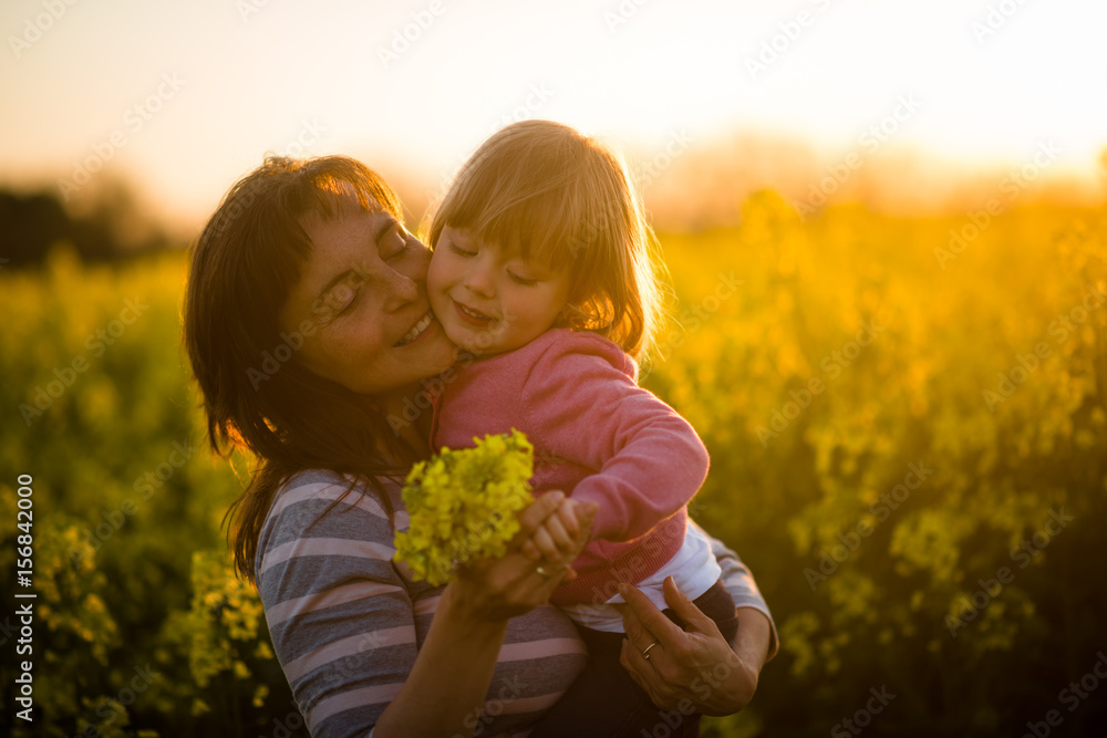 Mother with cute smiling daughter in the rapeseed field during sunset Mother with cute smiling daughter in the rapeseed field during sunset
