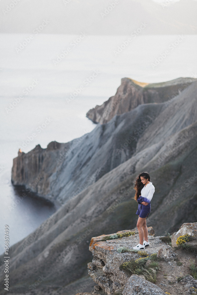 Woman standing on a cliff with a stunning view of sea coast with background of the hills and mountains. She is happy and enjoying the moment of freedom