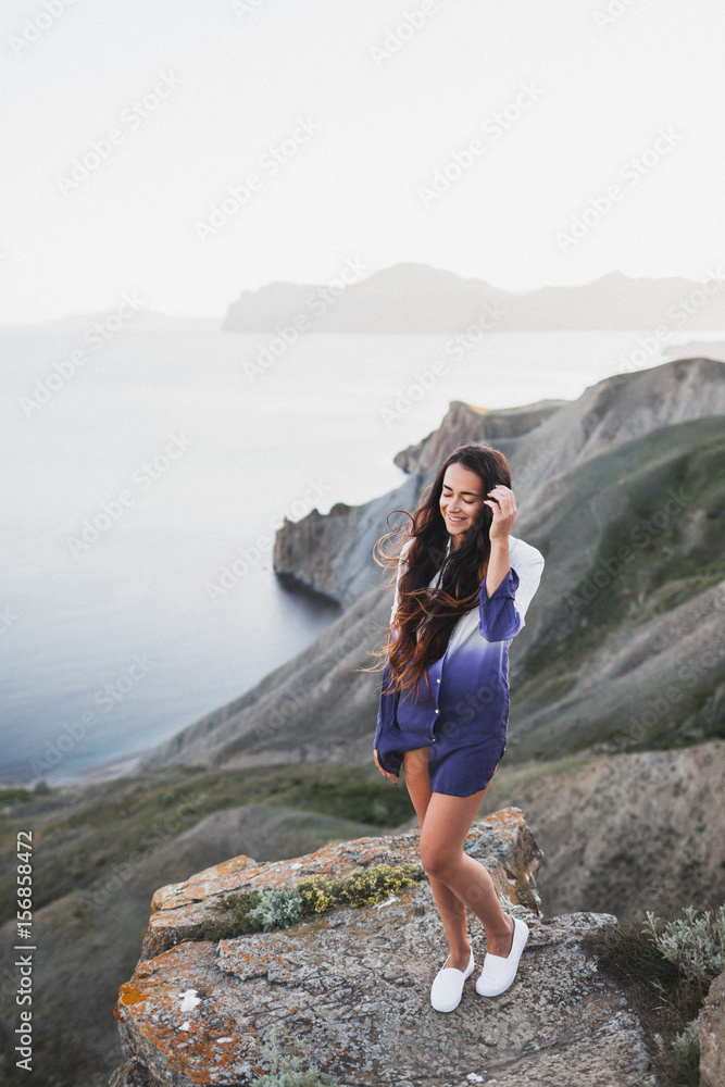 Naklejka premium Woman standing on a cliff with a stunning view of sea coast with background of the hills and mountains. She is happy and enjoying the moment of freedom