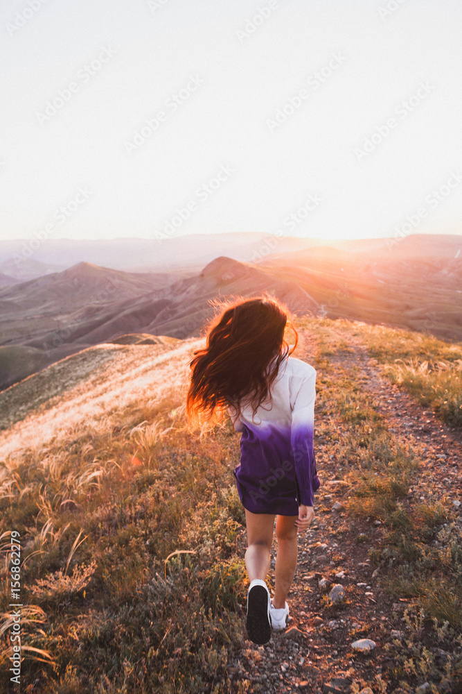 Happy young woman running on feather grass field in sunset light. Nature lifestyle and amazing view around. Long black hair with colored locks Happy young woman running on feather grass field in sunset light. Nature lifestyle and amazing view around. Long black hair with colored locks