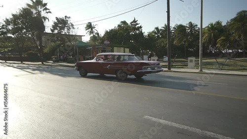 Red retro car convertible is riding on the central street of Varadero at sunset photo