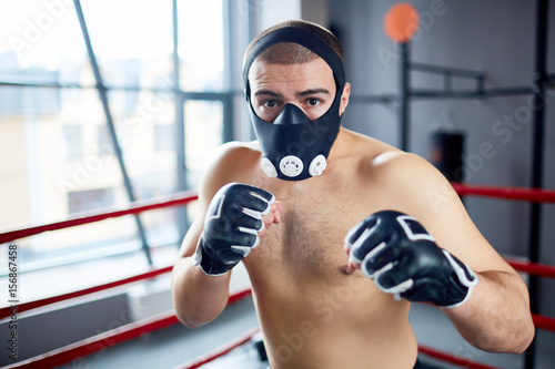 Strong kick-boxer in protective mask looking at his rival during attack