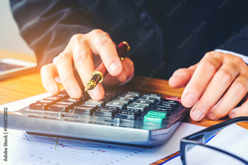 Fototapeta premium Businessman's hands with calculator at the office and Financial data analyzing counting on wood desk