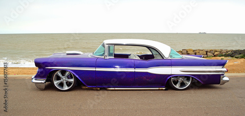 Classic  Purple American vintage car on seafront promenade, sea and beach in background. .
