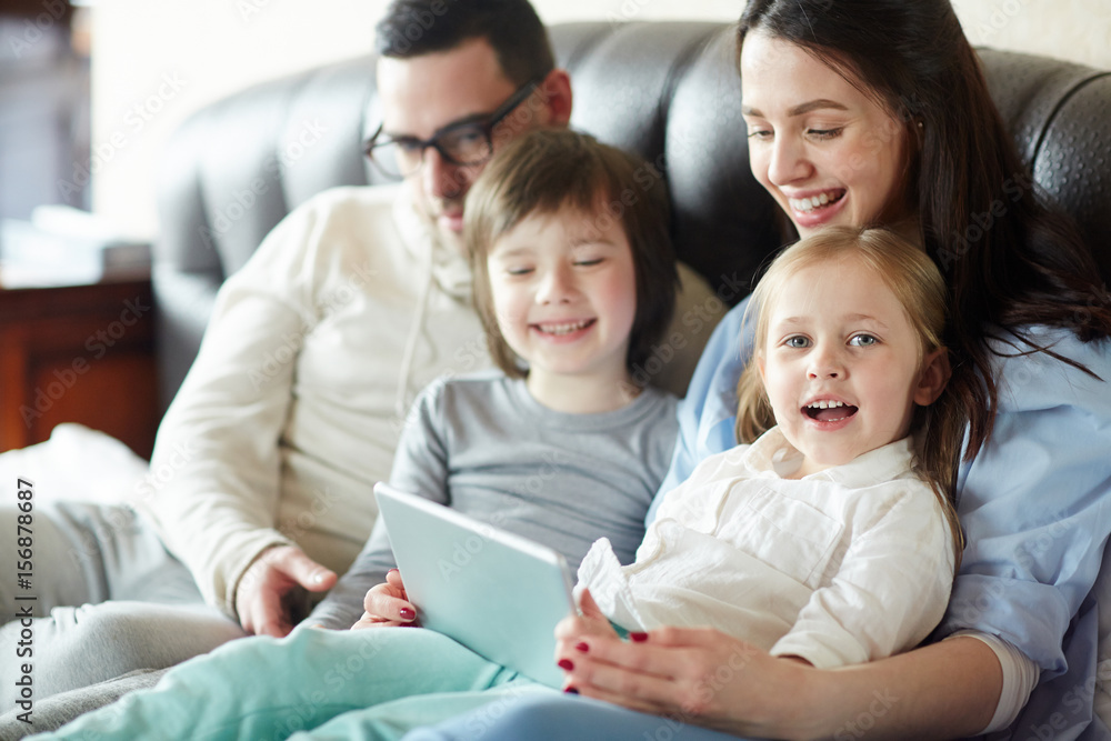 Happy family of four with touchpad sitting on sofa Happy family of four with touchpad sitting on sofa