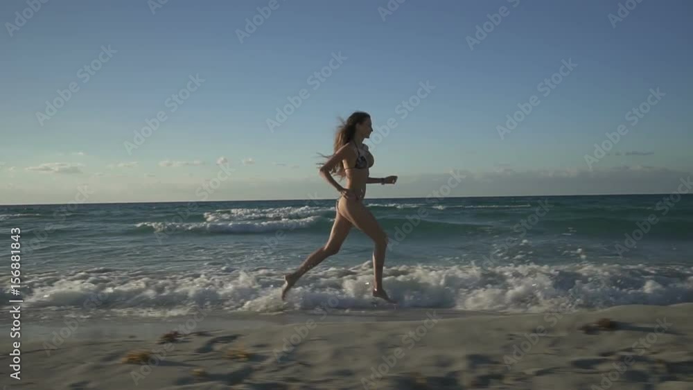 Beautiful young sporty woman is running along beach of caribbean coastline in sunset Beautiful young sporty woman is running along beach of caribbean coastline in sunset