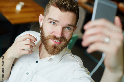 Portrait of handsome bearded man posing for selfie photo in cafe