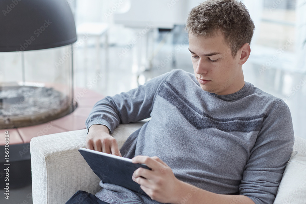 Attractive young Caucasian male relaxing at home with tablet, sitting on white sofa alone after work. Young hipster having video call with girlfriend, using online app on his modern gadget. Attractive young Caucasian male relaxing at home with tablet, sitting on white sofa alone after work. Young hipster having video call with girlfriend, using online app on his modern gadget.