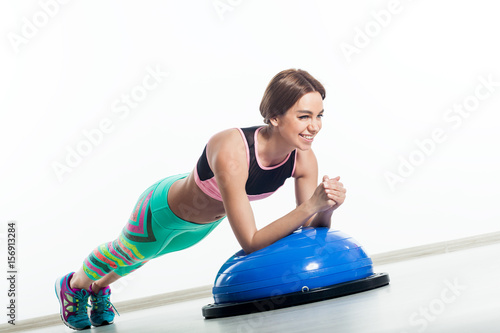 Young sportive woman smiling and doing exercises on blue bosu on isolated white background photo