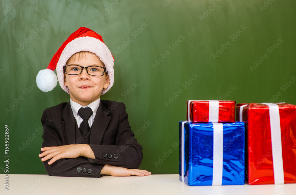 boy in red christmas hat with gift boxes near empty green blackboard boy in red christmas hat with gift boxes near empty green blackboard