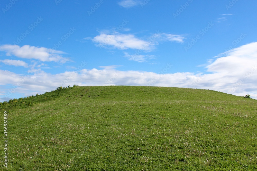 The grass hill with the clouds and the clouds in the background.