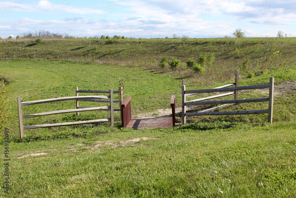 The wood fence and bridge in the green grass field.