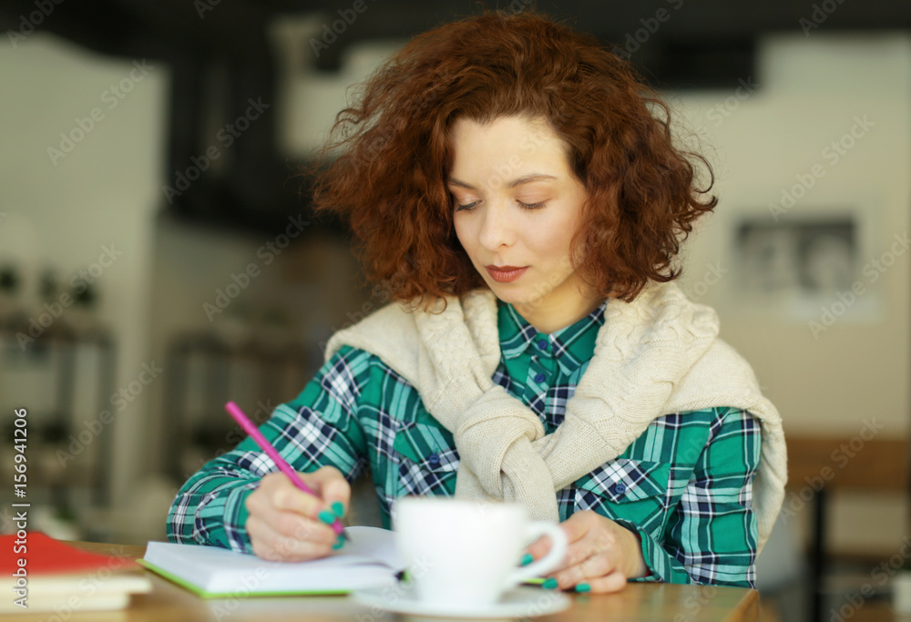 Beautiful girl writing in notebook in cafe Beautiful girl writing in notebook in cafe