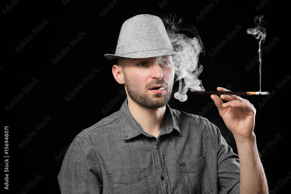 Handsome man smoking cigarette on dark background Handsome man smoking cigarette on dark background