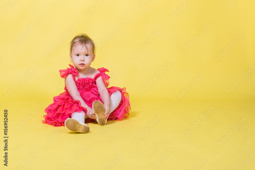 Girl toddler in a pink dress on a yellow background wearing the shoes on his feet Girl toddler in a pink dress on a yellow background wearing the shoes on his feet
