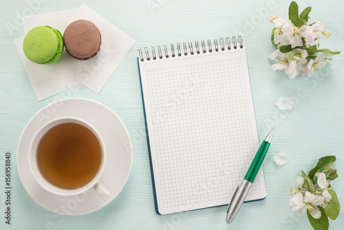 Notepad, pen, flowers, and macarons with cup of tea