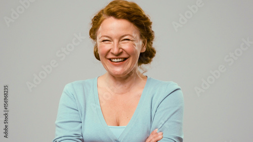 Mid aged actress showing emotions of joy. Actress in studio shows the emotion of joy. Close up portrait of an actrees in light blue jumper. Actress with curly red hair shows the emotion of joy photo