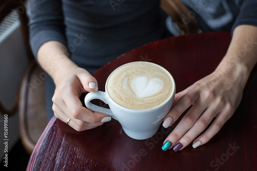 Hands holding cup of coffee with foam and heart