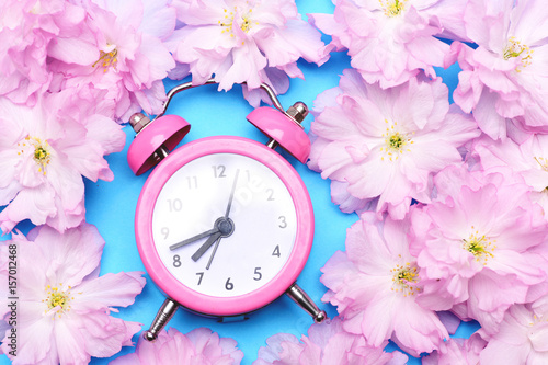 Alarm clock in bright pink colour surrounded with pink sakura