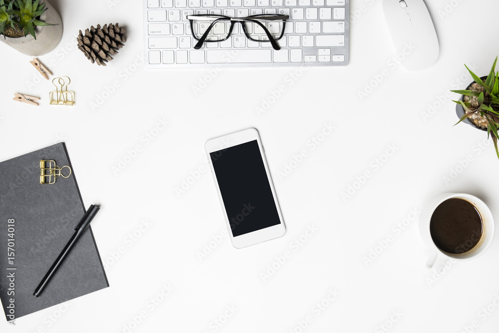 White smartphone with blank screen is on top of white desk table. Top view, flat lay. White smartphone with blank screen is on top of white desk table. Top view, flat lay.