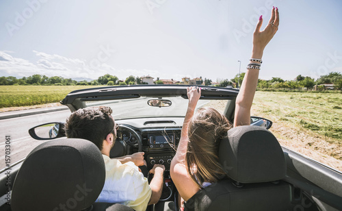 Traveller happy couple driving on the road into in a sports car rasing their arms to the sky photo