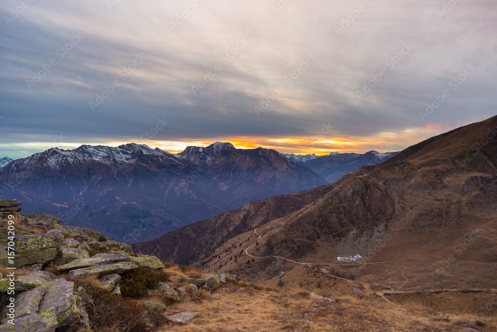 Plakat Ostatnie ciepłe światło słoneczne w alpejskiej dolinie ze świecącymi szczytami górskimi i malowniczymi chmurami. Włoskie Alpy Francuskie, cel podróży letnich.