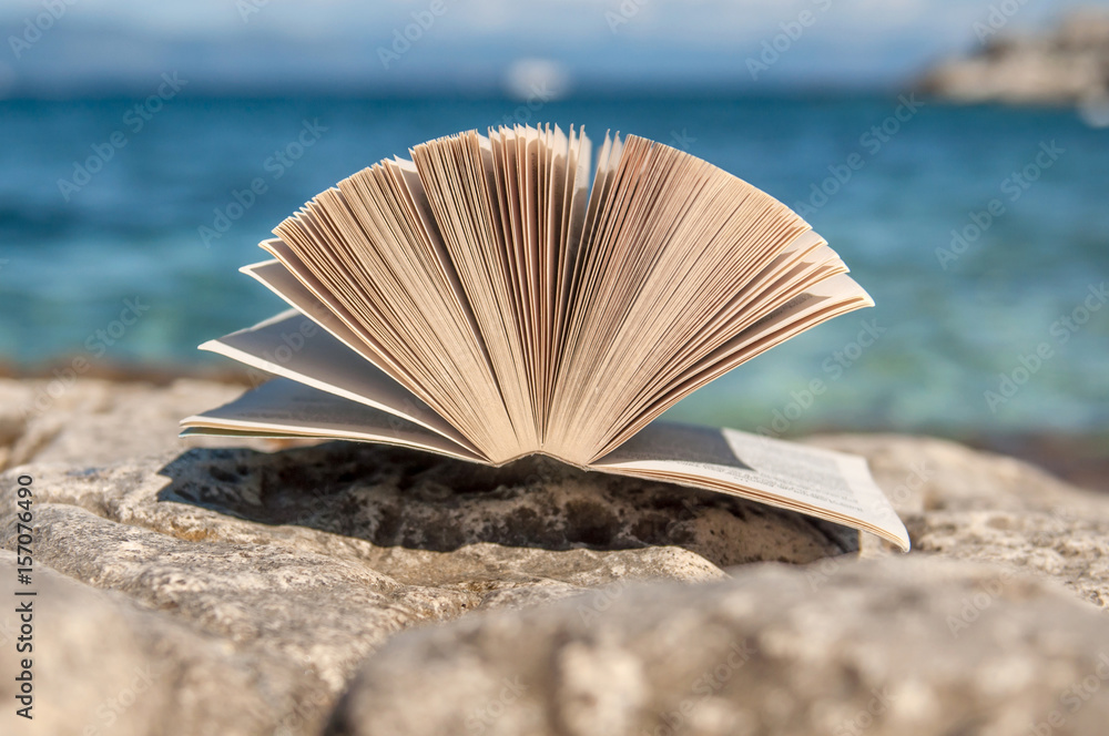 Open book at beach near the sea during bright sunny summer holiday vacation day Open book at beach near the sea during bright sunny summer holiday vacation day