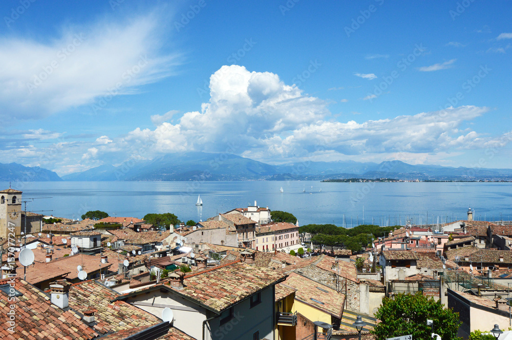 DESENZANO DEL GARDA, ITALY - MAY 15, 2017: amazing panorama from Desenzano castle on Lake Garda with old city roofs, mountains, white clouds and sailboats on the lake, Desenzano del Garda, Italy