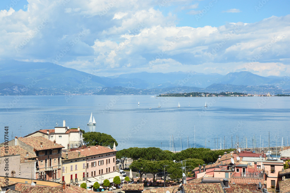 DESENZANO DEL GARDA, ITALY - MAY 15, 2017: amazing panorama from Desenzano castle on Lake Garda with old city roofs, mountains, white clouds and sailboats on the lake, Desenzano del Garda, Italy