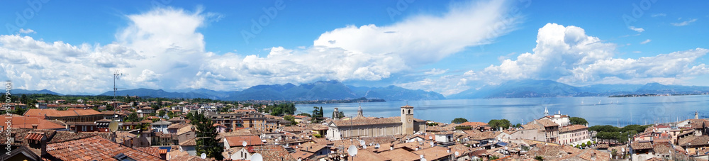 Amazing panoramic view from Desenzano castle on Lake Garda with old city roofs, mountains, white clouds and sailboats on the lake, Desenzano del Garda, Italy