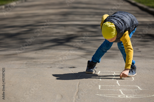Kid boy drawing hopscotch on asphalt. Child playing hopscotch on playground outdoors on a sunny day. outdoor activities for children.