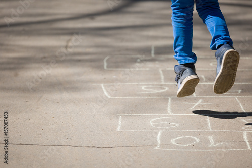 Closeup of boy's legs and hopscotch drawn on asphalt. Child playing hopscotch on playground outdoors on a sunny day. outdoor activities for children.
