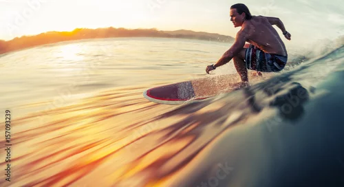 Obraz Surfer jeździ na fali oceanu o wschodzie słońca