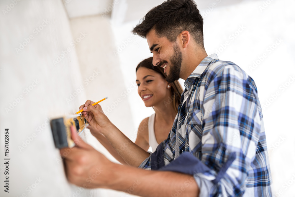 Smiling young couple measuring wall whit level tool, renovation concept - obrazy, fototapety, plakaty 