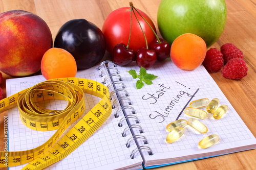 Fresh fruits, tablets supplements and centimeter with notebook, concept of slimming and healthy food