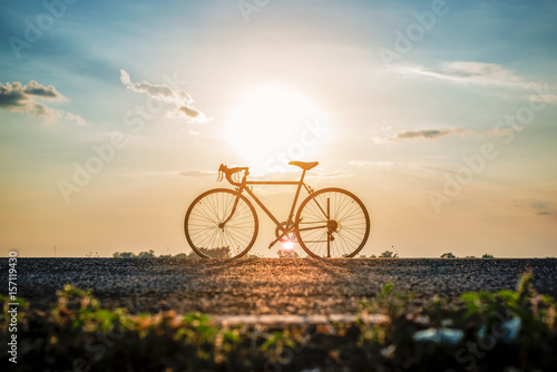 Silhouette of bicycle on the road in front of sunset background. © paejar