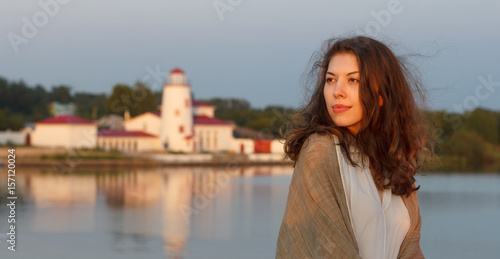 Cute young woman resting on the banks of the river at sunset.