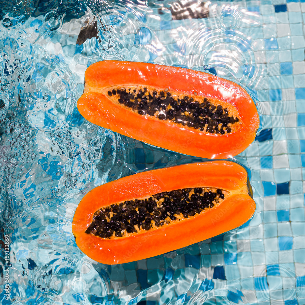 In the pool on the water floats two halves of cut papaya. Tropical fruits, healthy diet, top view In the pool on the water floats two halves of cut papaya. Tropical fruits, healthy diet, top view